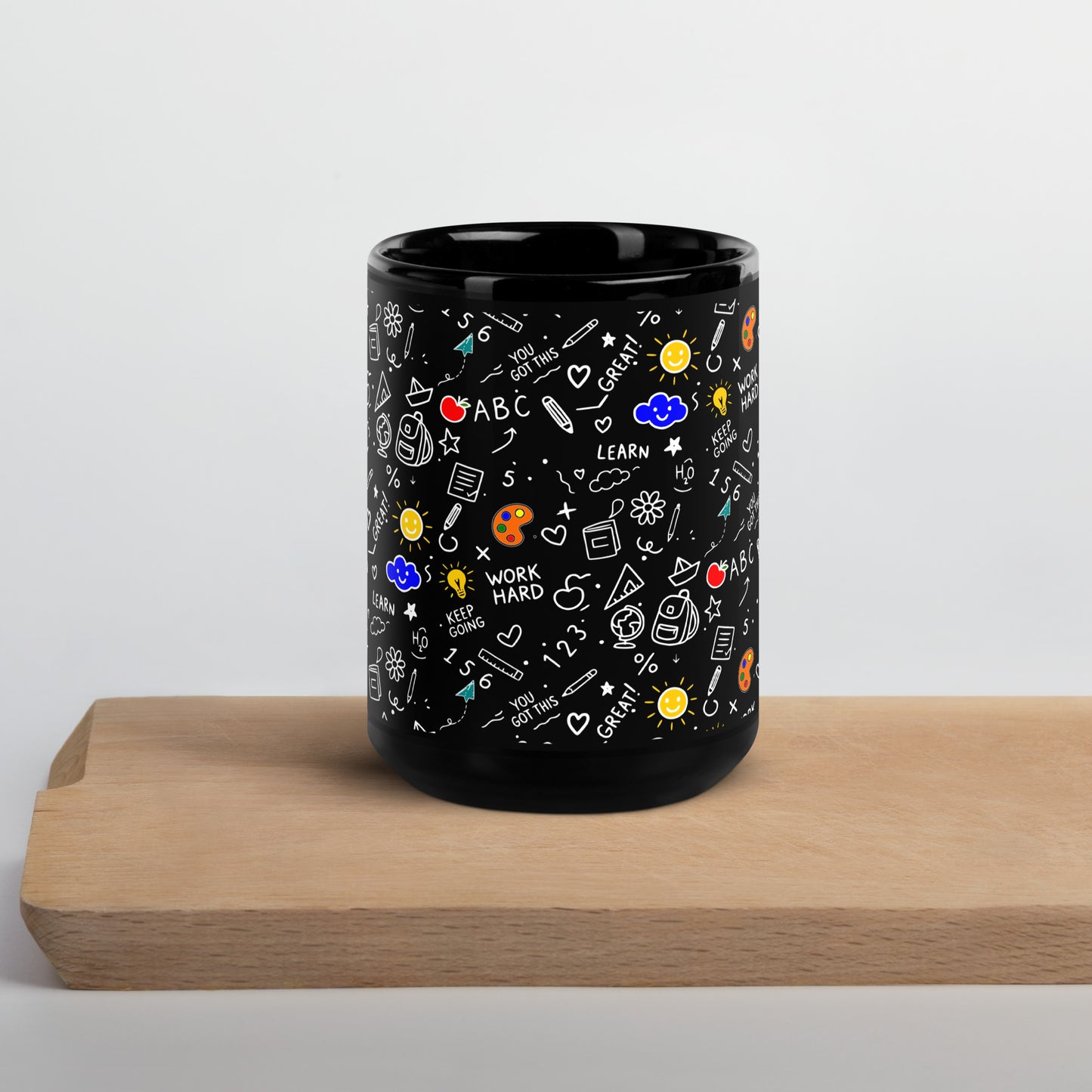 Black glossy ceramic mug with hand-drawn school doodle illustration — books, pencils, numbers and happy faces on a bold dark finish