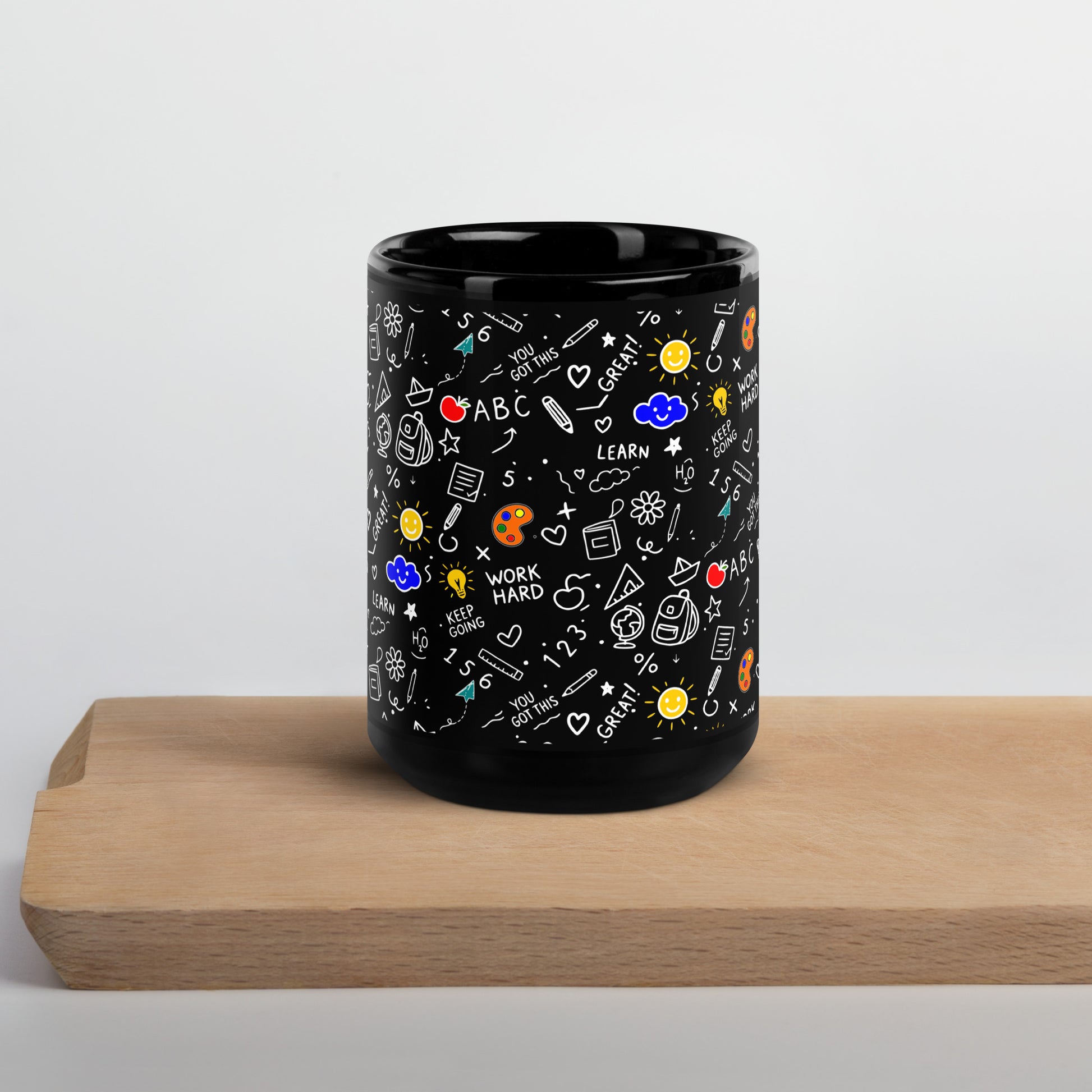 Black glossy ceramic mug with hand-drawn school doodle illustration — books, pencils, numbers and happy faces on a bold dark finish