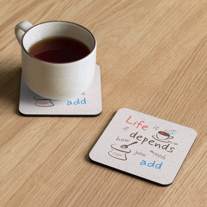 Square cork-back coaster printed with "Life is coffee — it depends how much sugar you add," featuring playful color accents and a speckled background design, shown on a flat surface.