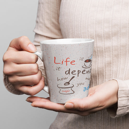 12oz white ceramic latte mug printed with "Life is coffee — it depends how much sugar you add," featuring playful color accents and a speckled background design.
