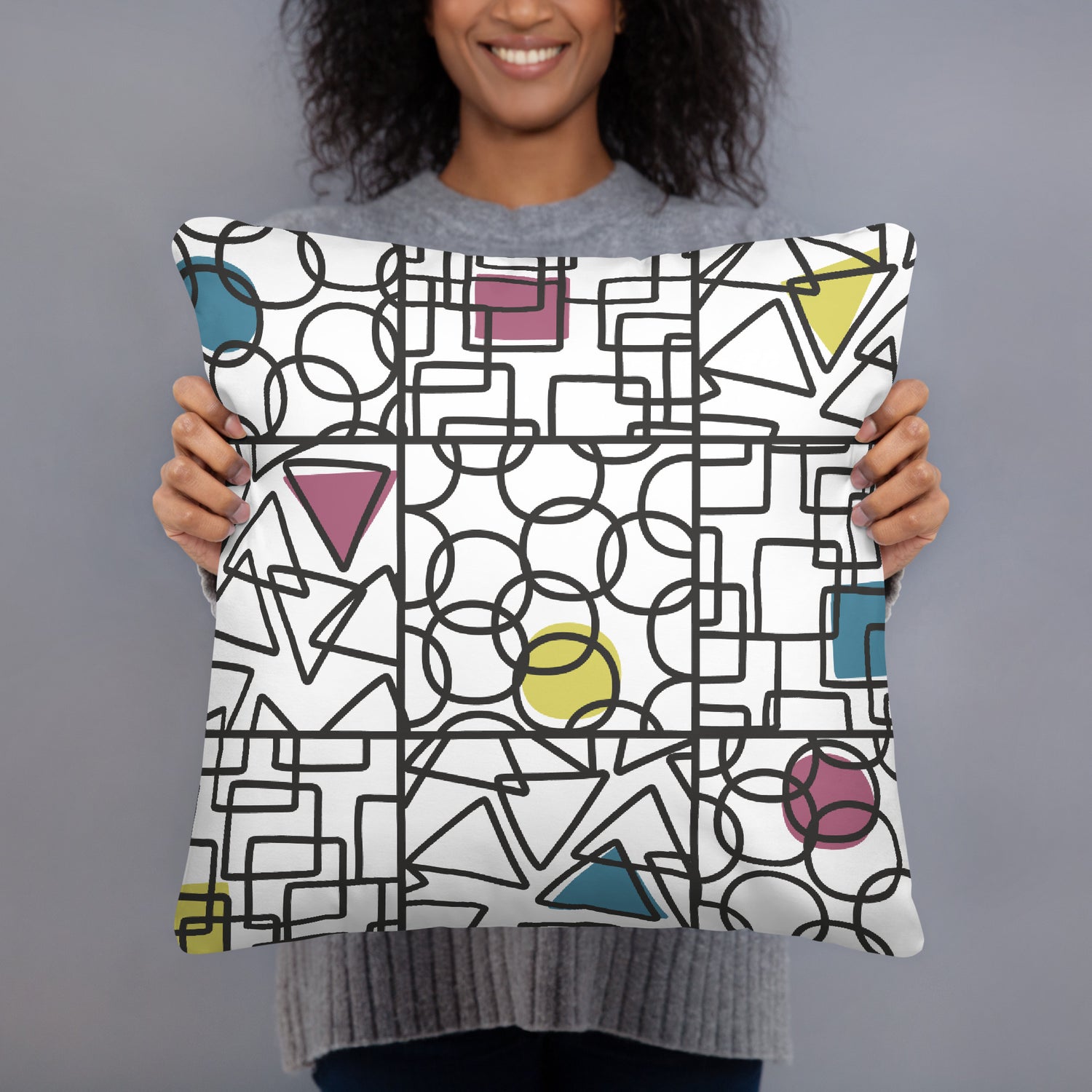 White accent pillow printed with a bold repeating geometric pattern of circles, triangles and squares in cyan, magenta, yellow and black. Shape. Check. Repeat. by MWL.