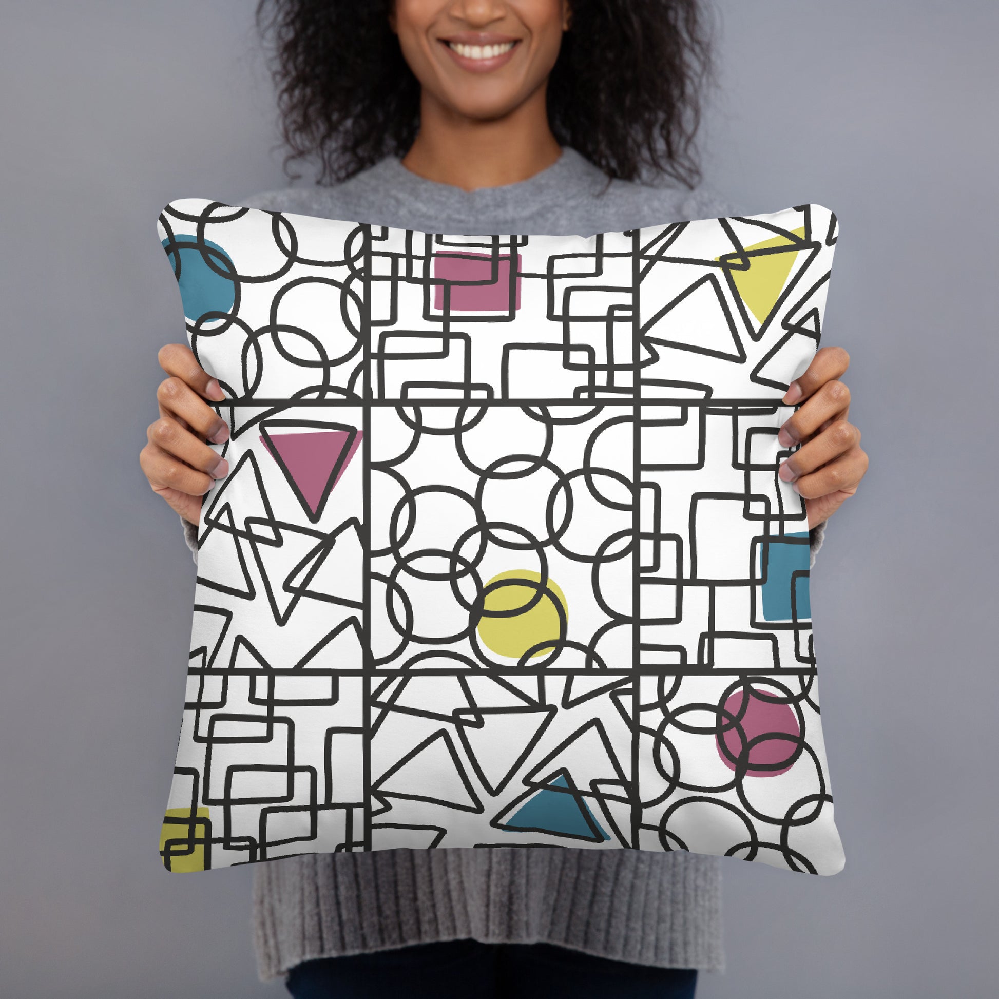 White accent pillow printed with a bold repeating geometric pattern of circles, triangles and squares in cyan, magenta, yellow and black. Shape. Check. Repeat. by MWL.